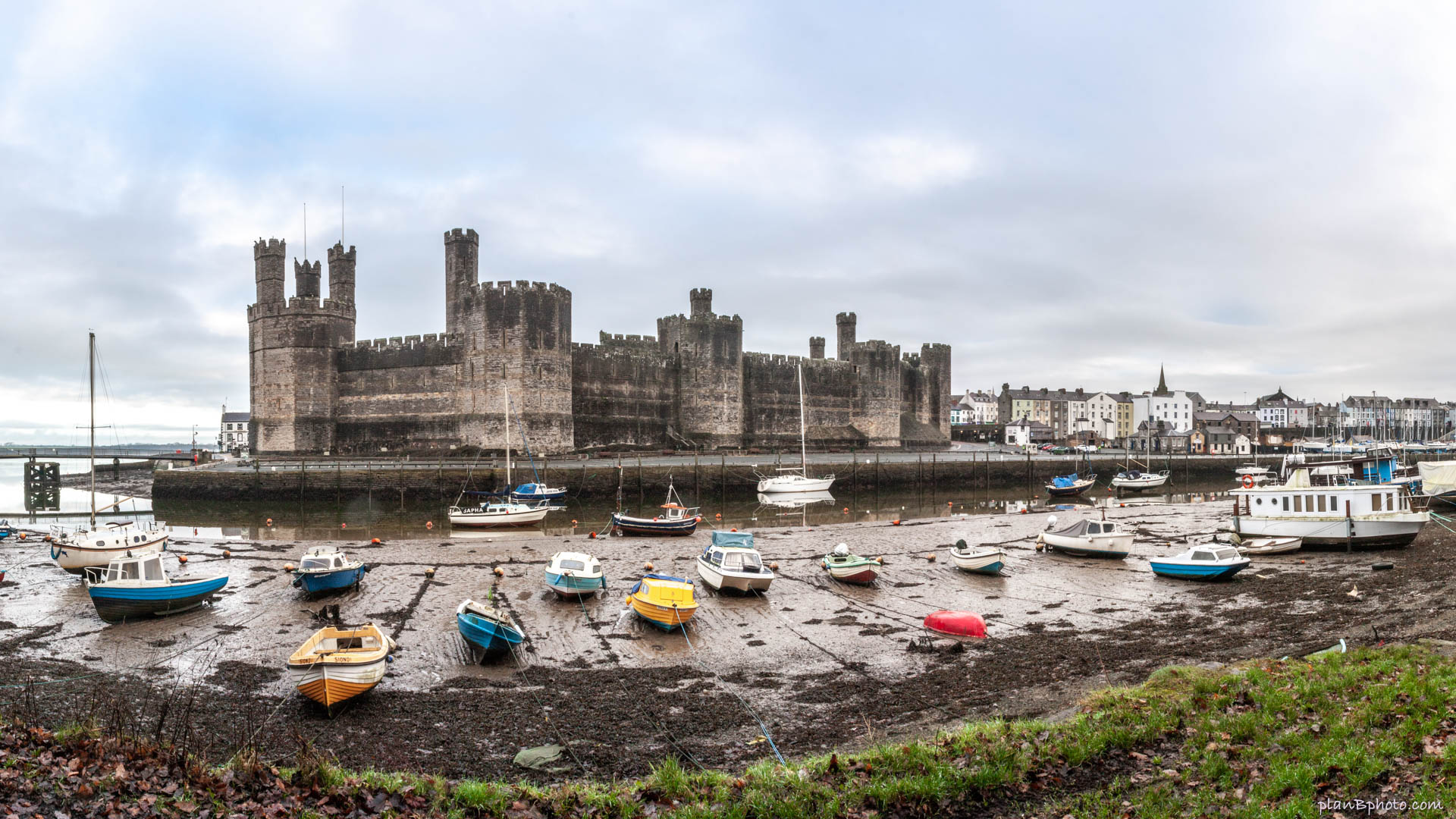 Caernarfon castle in the morning with boats in low tide