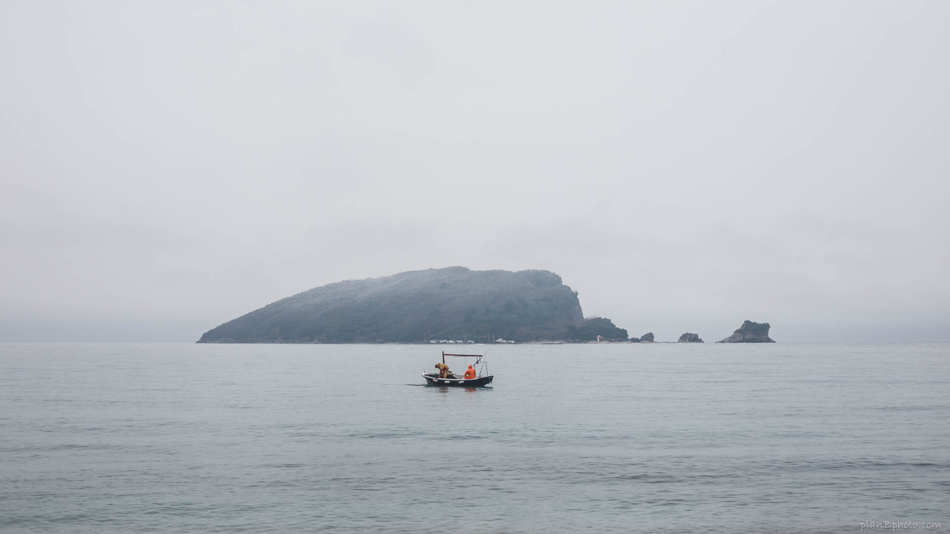 Two fisherman at sea in a boat near an island in foggy weather