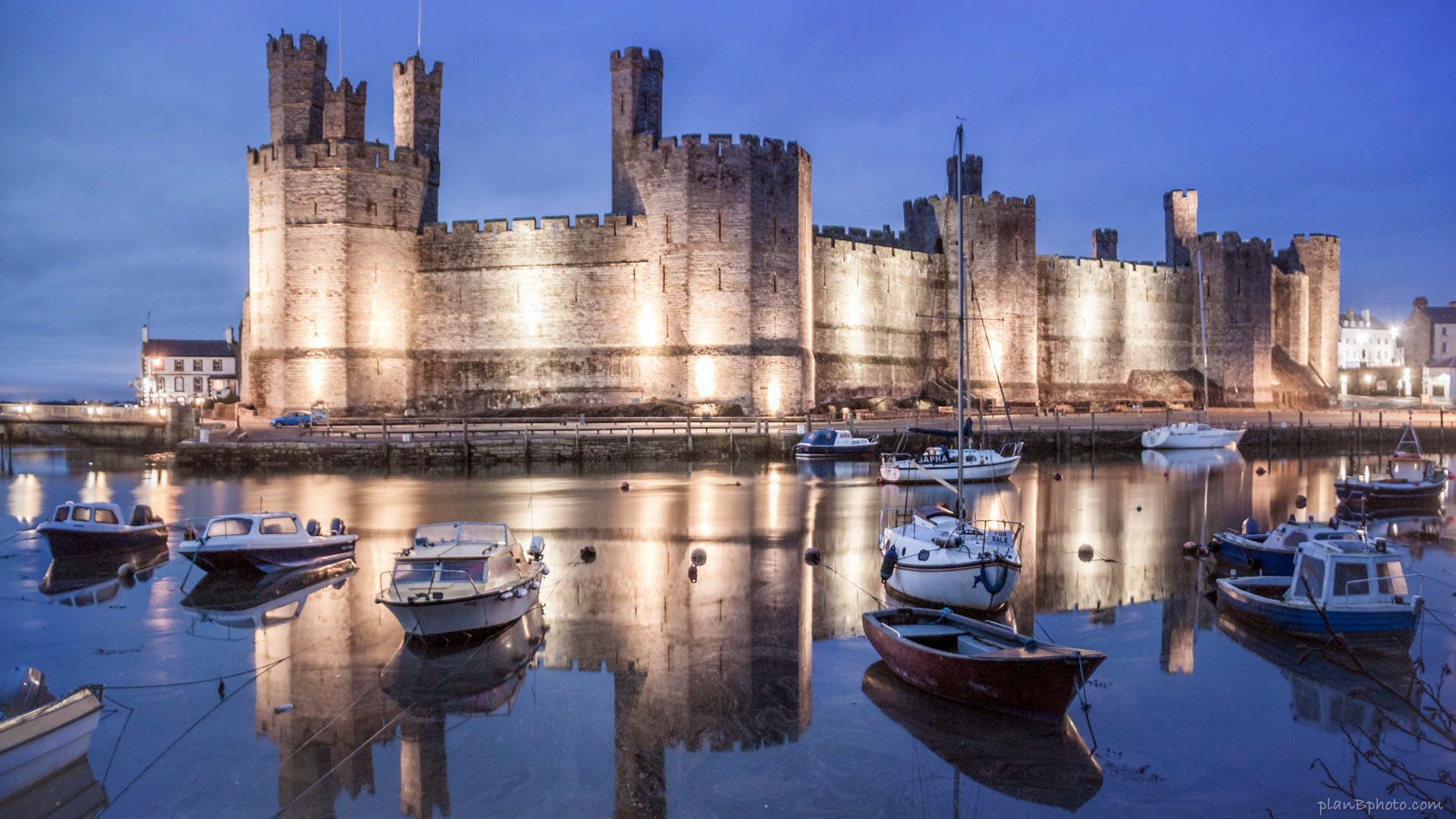 Caernarfon Castle in Wales at night with boats floating in river in front of it